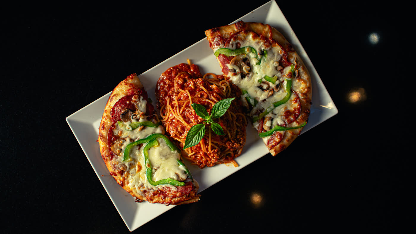 Pizza and spaghetti, shot from above on a dark table