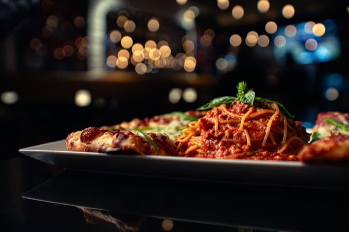 Spaghetti and pizza at table level, bokeh lights behind